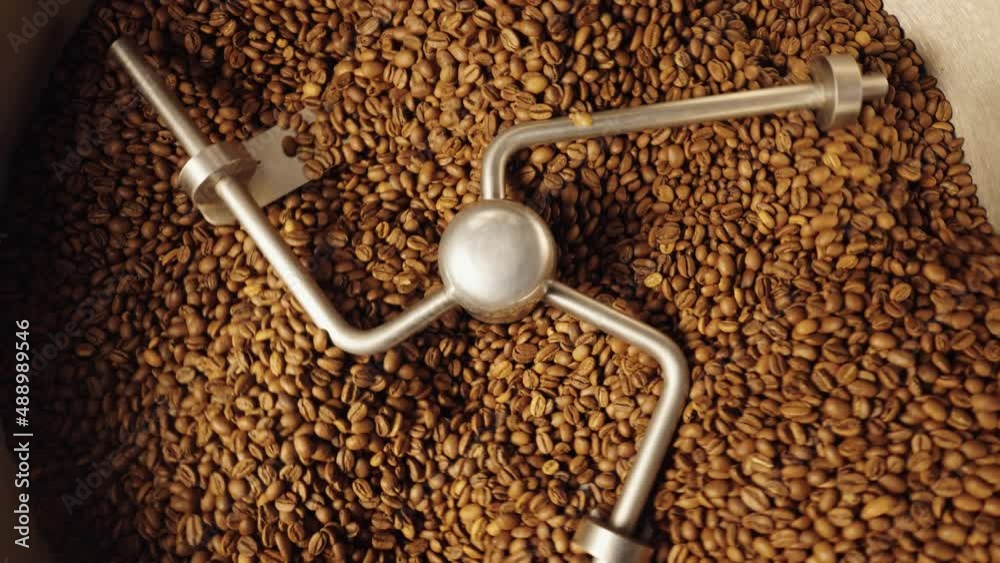 Top view of industrial mixing machine mixes roasted coffee beans in roaster, close up. Roasting process in coffee roasting machine in factory. Food and drink background for cafe. Slow motion.