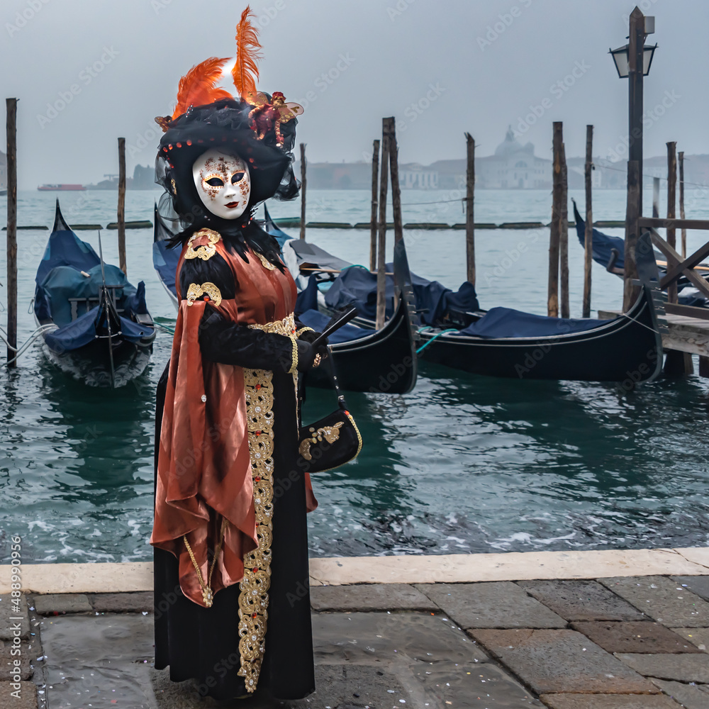 Karneval in Venedig, Dame im Kostüm mit Maske und Feder auf dem Hut vor Gondeln