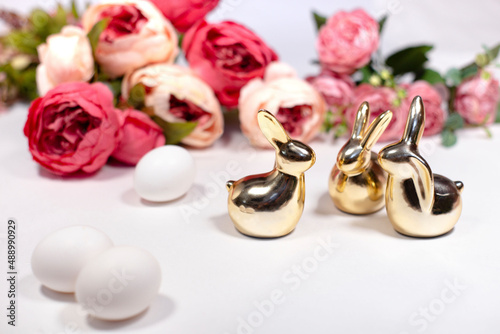 three golden rabbits behind white background with flowers