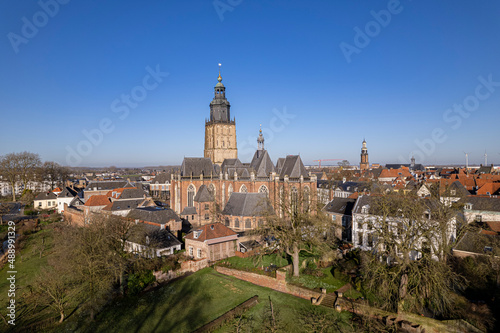 Medieval city wall and authentic historic tower town Zutphen gardens with Walburgis church towering over the medieval rooftops against a clear blue sky