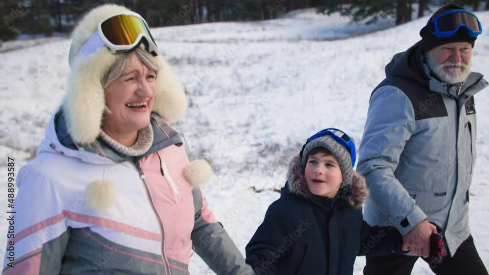 pensioners laugh and talk with their grandson during walk, child boy tells stories to grandparents holding hands in the winter forest pensioners laugh and talk with their grandson during walk, child boy tells stories to grandparents holding hands in the winter forest