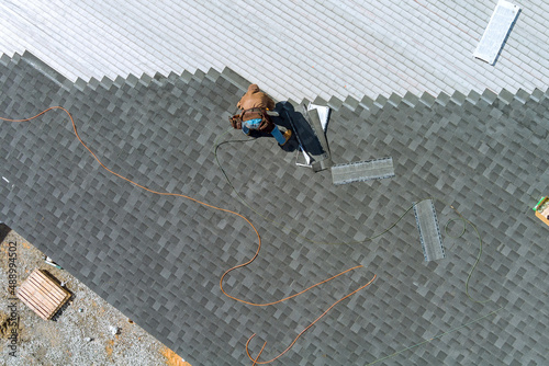 A asphalt shingles installation on the roof roofer is nailing asphalt shingles to roofing construction