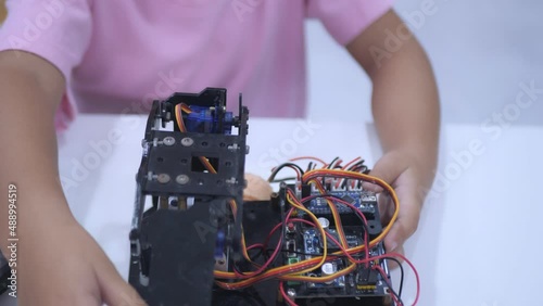 Slow motion scene of Asian girls in glasses holding a robot. A girls in a pink shirt and glasses sits at a table in front of him having a robot made by a girls. He is very satisfied with his work.