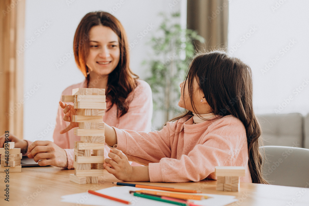 Mother with daughter building wooden jenga blocks into tower