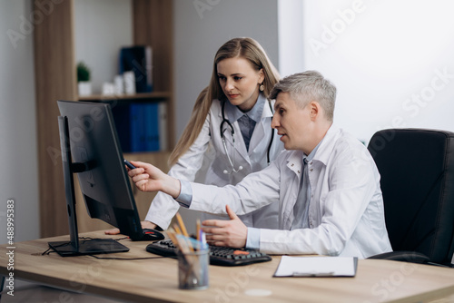 Two doctors talking at workplace looking at computer screen, analyzing results of patients medical examination, feeling satisfied with good news.