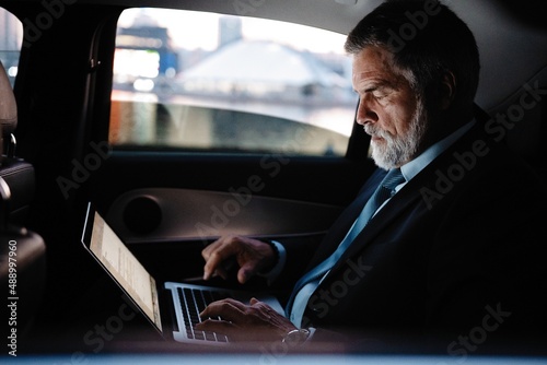 Full concentration at work. Confident mature man in full suit working using laptop while sitting in the car. © opolja