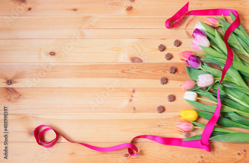 Colorful spring tulip flowers and chocolate candies as border on wooden background.