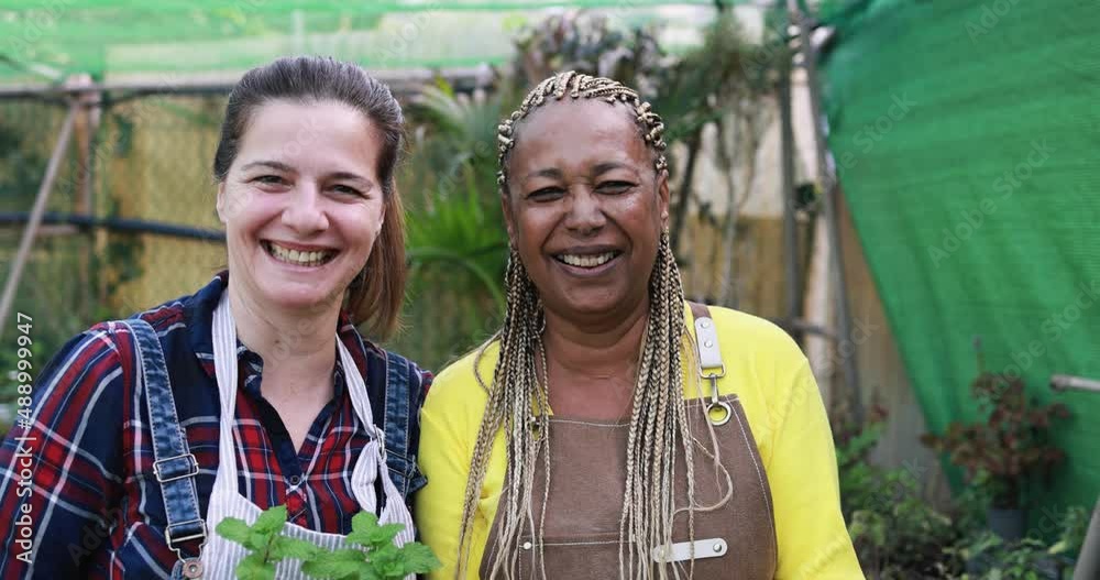 Multiracial senior women working inside greenhouse garden while smiling on camera