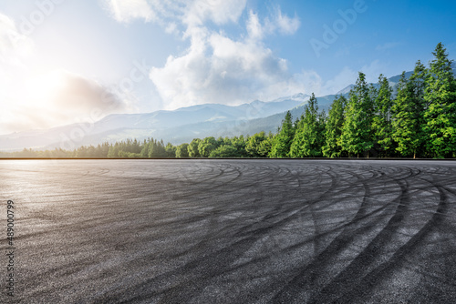 Empty asphalt road and green forest with mountain scenery at sunrise