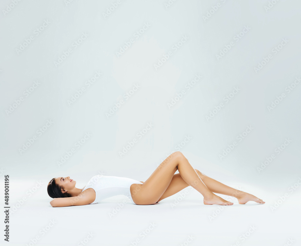 Young, fit and beautiful brunette woman in white swimsuit posing in studio. Concept of fitness, dieting and skin care. Young, fit and beautiful brunette woman in white swimsuit posing in studio. Concept of fitness, dieting and skin care.