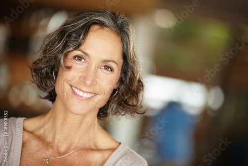 Laughter kept her heart young. A mature woman smiling happily while standing indoors at home.