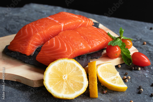 Salmon. Fresh raw salmon fish. Raw salmon fillet with pepper, herbs, lemon, tomato ingredients for cooking on black stone table rustic style. Top view with copy space.