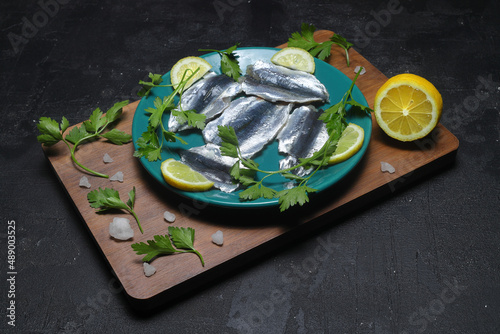 Fototapeta Naklejka Na Ścianę i Meble -  Sardines with lemon, salt and parsley close-up on a dark background. Sea fish. Top view.