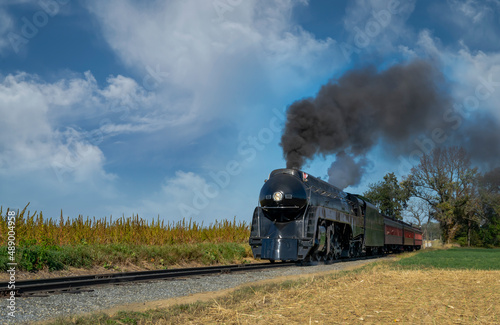 An Antique Restored Steam Engine Approaching Head-on, On Some Old Rail Road Tracks Blowing Smoke and Steam Traveling thru Farmlands.