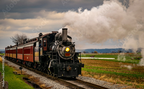 A Antique Restored Steam Engine and Coaches Approach Blowing Smoke and Steam Passing Thru Corn Fields on a Sunny Day