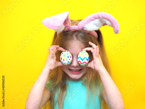 Closeup portrait of a little girl on a yellow background with an easter colored egg. Cute happy cheerful beautiful charming child in a bunny costume.
