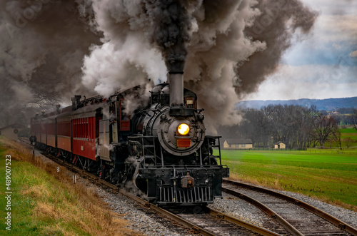 An Antique Steam Passenger Train Traveling Thru Farmlands Puffing Lots of Smoke on a Cloudy Winter Day