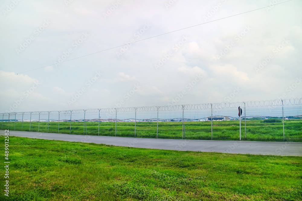 Road Outside Airport Lined by a Wire Fence with green grass and brigth sky
