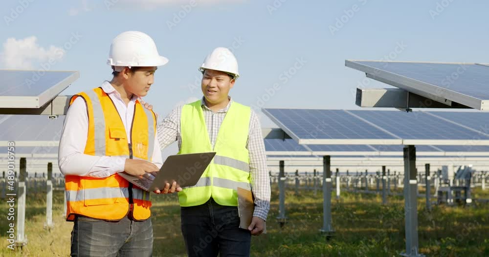 Asian Inspector Engineer man Holding checking board and young specialist man use laptop computer, Two engineers are discussing during working at solar farm, solar panel station in background Asian Inspector Engineer man Holding checking board and young specialist man use laptop computer, Two engineers are discussing during working at solar farm, solar panel station in background