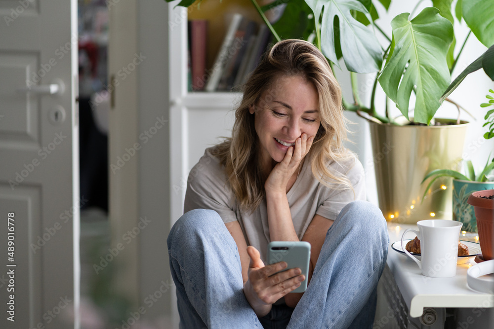 Fototapeta premium Happy pleasant middle age Swedish female using mobile smart phone, talking in video chat with friend, chatting in social media, shopping online, buying in internet, ordering products online in apps