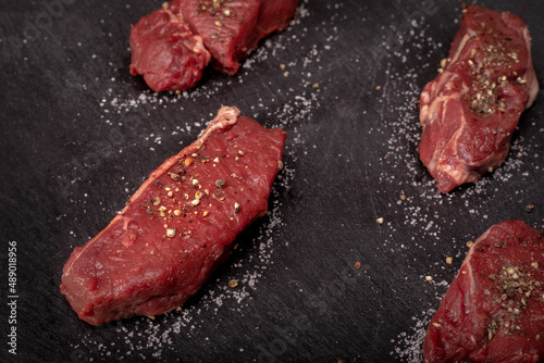 Raw beef tenderloin with salt and pepper on a black background, blackboard. Beef, game meat steaks. Red meat chops.