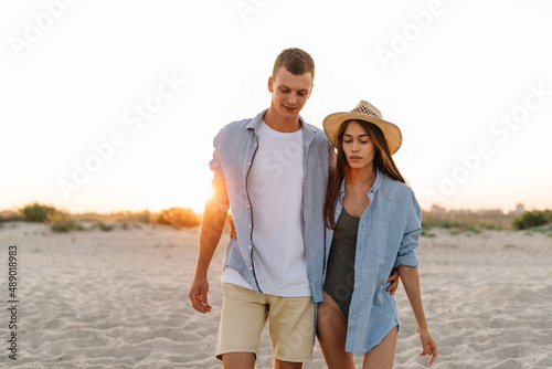 Back rear view young happy couple two friends family man woman in white shirt clothes hold hands walk run stroll together at sunrise over sea beach ocean outdoor exotic seaside in summer day evening