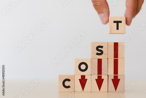 Cost reduction concept. Lean manufacturing management. Decreasing company expense to maximize profits. Hand puts wooden cube with text “cost” with red down arrows .Business survival and improvement.