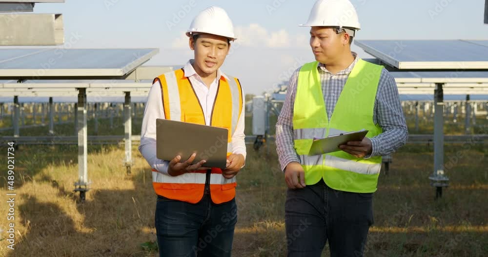 Asian Inspector Engineer man Holding checking board and young specialist man use laptop computer, Two engineers discussing and glad in success during working at solar farm, solar panel in background Asian Inspector Engineer man Holding checking board and young specialist man use laptop computer, Two engineers discussing and glad in success during working at solar farm, solar panel in background