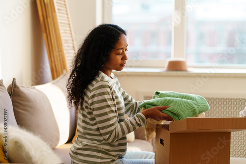 Fotografie Young african-american female packing stuff in cardboard box
