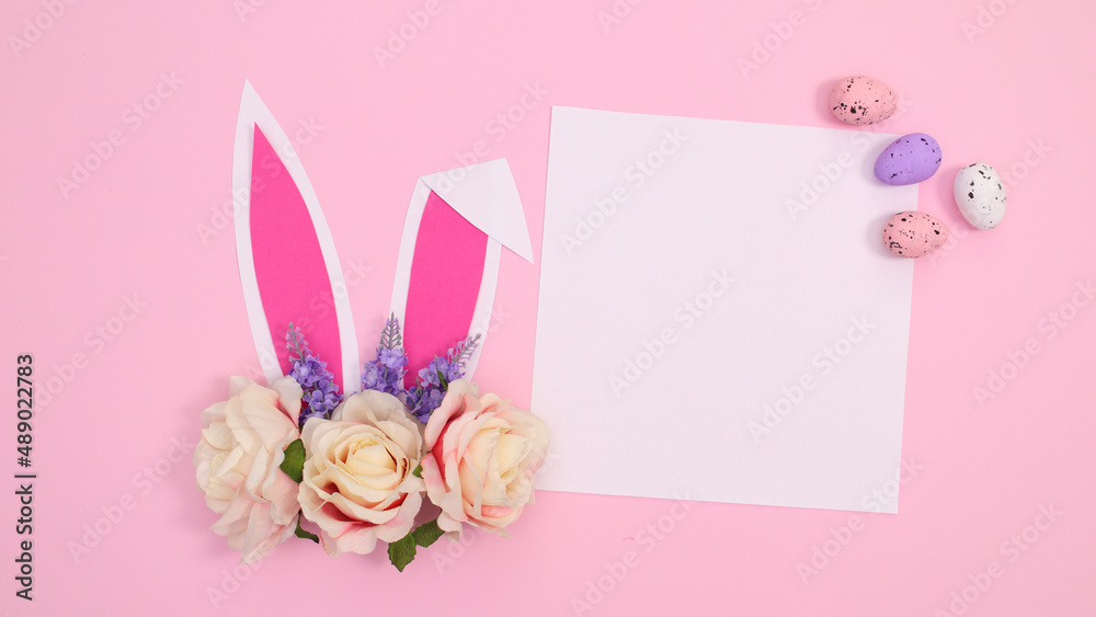 Spring holidays creative paper card copy space with bunny ears with bloom flowers on pastel pink background. Creative Easter concept