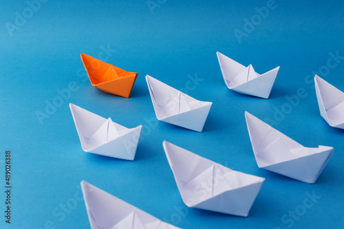 Business Leadership Concept - Orange Color Paper ship Origami leading the rest of the white paper ship on blue background.
