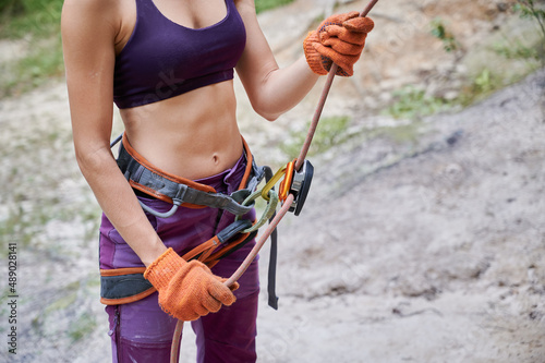 Close up of young female climber belaying leader during rock climbing outdoors, using rope, grigri, carabines and gloves. Concept of teamwork, trust, extreme sport and outdoor activity. photo