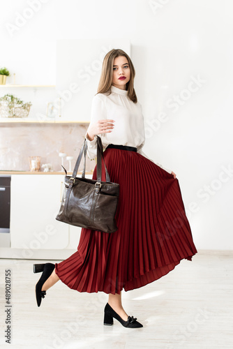 Portrait of fashionable women in a red skirt, white blouse and stylish suedeshoes with a buckle posing on the kitchen photo