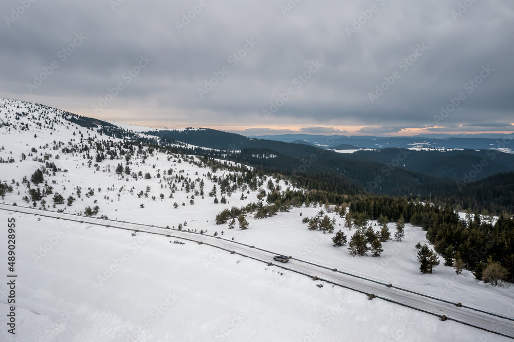 Aerial drone photography of a snowy mountain with a car on the road. Winter landscape countryside.