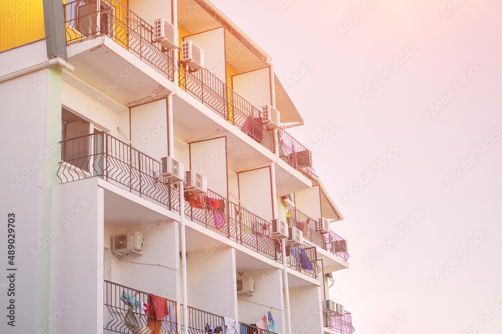 Resort hotel, on the balconies of which numerous towels and other clothes of guests are dried. In the frame is part of the facade of the boarding house on a sunny day. Orange tint