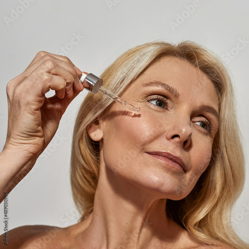 Woman drip cosmetic oil with dropper on her face
