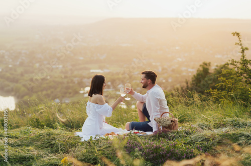 Summer picnic in the mountain. Young romantic couple in love clinking glasses outdoors. Leisure, food and drinks concept. 