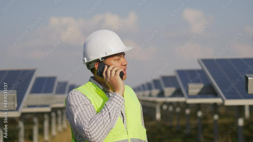 Seriously Asian technician man standing and talking on smartphone between long rows of photovoltaic solar panels Seriously Asian technician man standing and talking on smartphone between long rows of photovoltaic solar panels