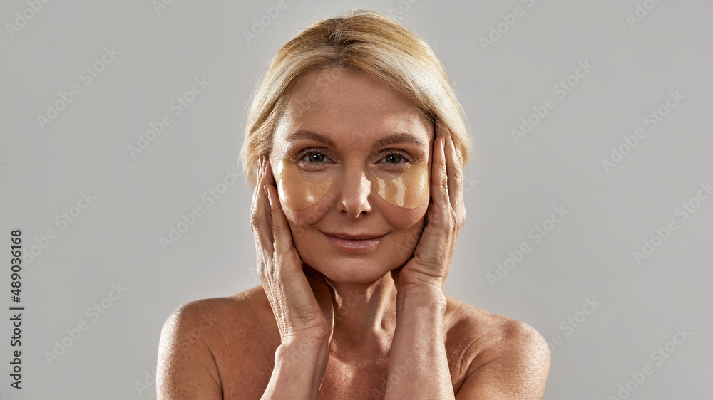 Mature woman touching face with under eye patches Mature woman touching face with under eye patches