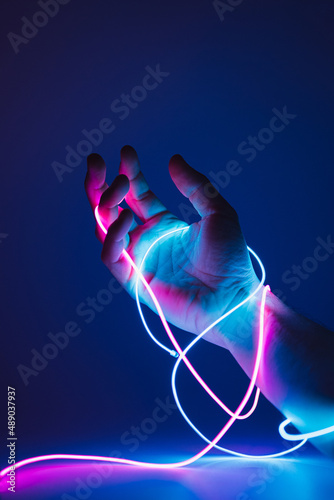 Hand tied with neon led cables on a dark background. Immersive reality concept.