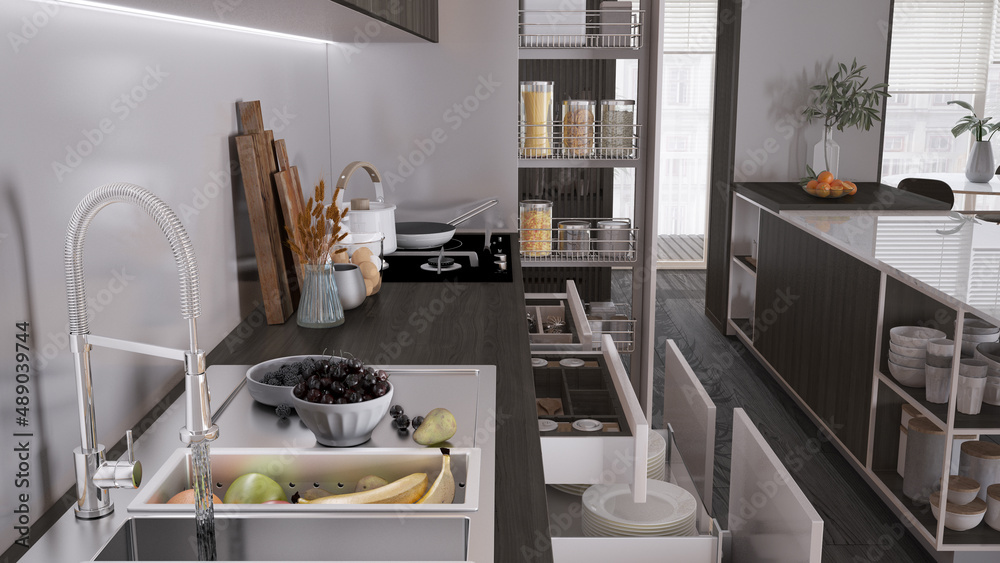 Cozy dark wooden kitchen close up, open drawers with pottery and utensils. Sink with fruit, induction hob with pots, wooden cutting boards. Contemporary interior design concept Cozy dark wooden kitchen close up, open drawers with pottery and utensils. Sink with fruit, induction hob with pots, wooden cutting boards. Contemporary interior design concept