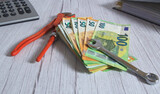 Ein Stapel Geldscheine mit Schraubenschlüssel und Rohrzange auf Holzuntergrund, horizontal