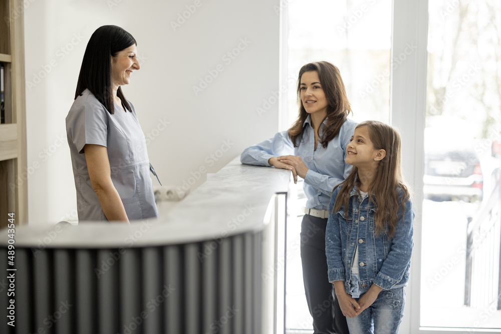 Φωτογραφία Young woman with little girl talking with medical worker at the reception desk of the clinic