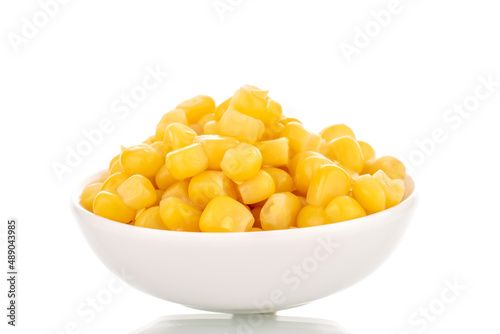 Bright yellow canned corn kernels in white ceramic saucer, macro, isolated on white background.