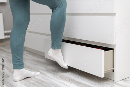 a female leg pushes a drawer of chest of drawers with her foot closing it photo