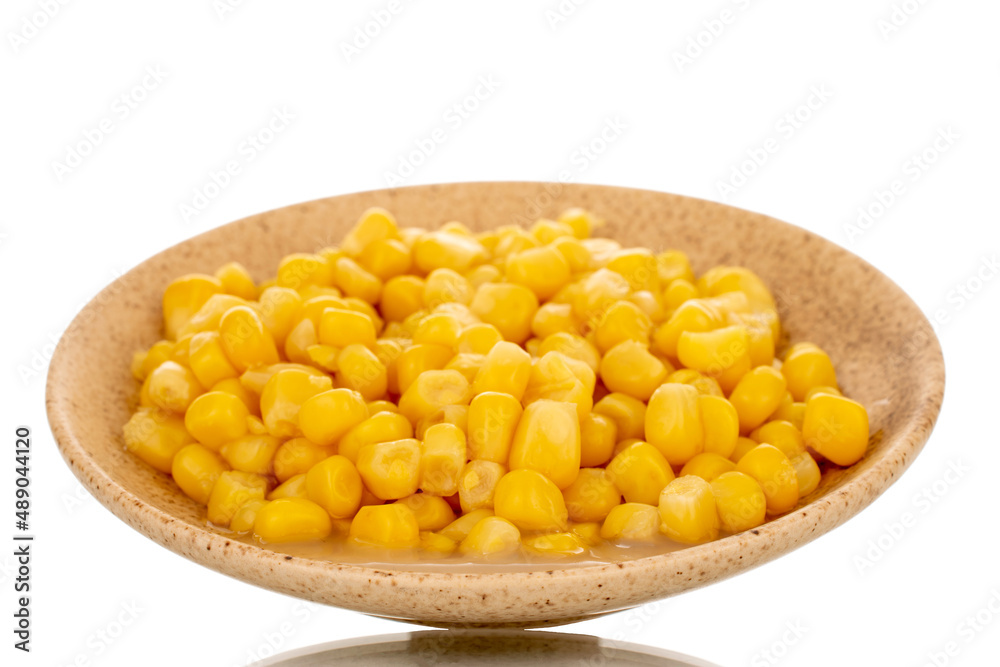 Bright yellow canned corn kernels in white ceramic saucer, macro, isolated on white background. Bright yellow canned corn kernels in white ceramic saucer, macro, isolated on white background.