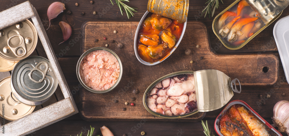 Φωτογραφία Various delicious canned fish and seafood in aluminum cans on the dark wooden background