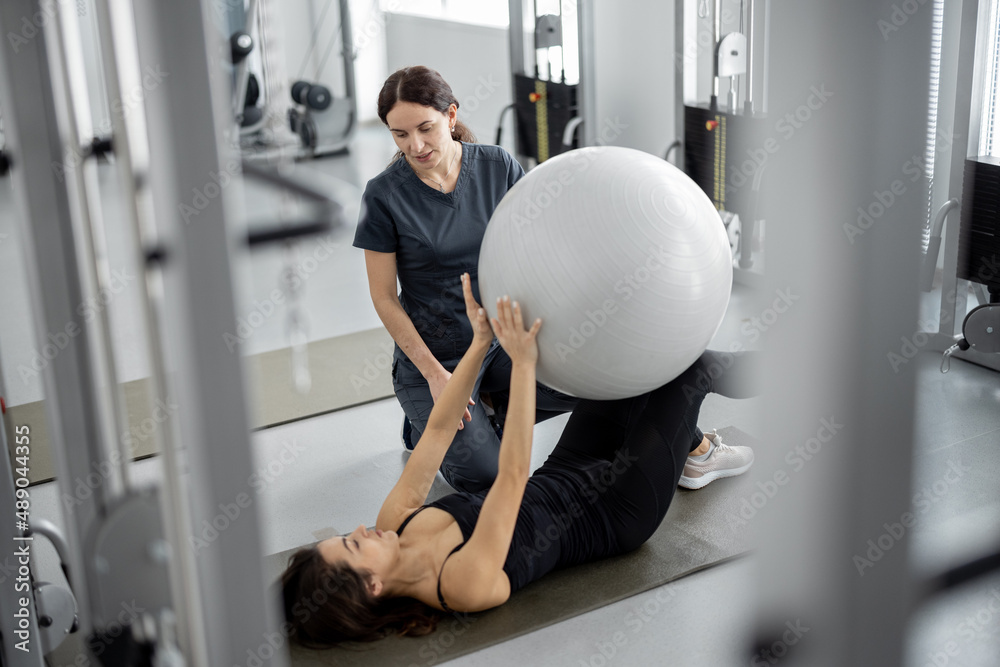 Φωτογραφία Woman doing exercises with fitness ball with rehabilitation specialist at the gym