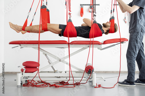 Male patient hanging on suspensions at rehabilitation center. Therapeutic exercises and neuromuscular activation on red cord slings photo