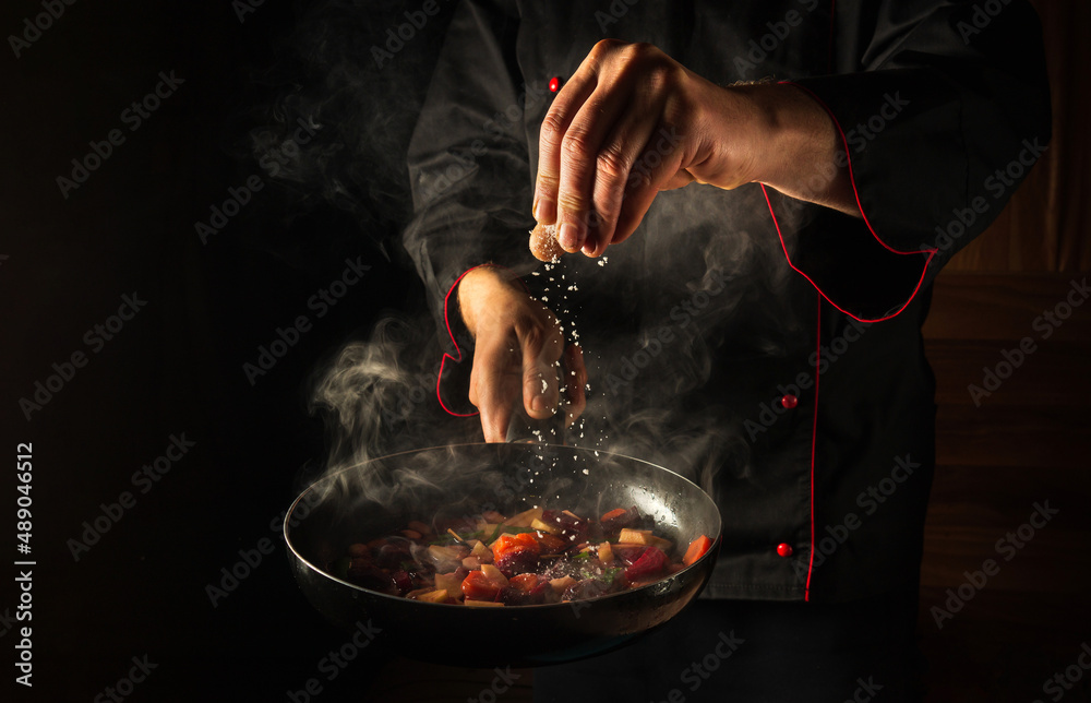 Cooking fresh vegetables. The chef adds salt to a steaming hot pan. Grande cuisine idea for a hotel with advertising space - obrazy, fototapety, plakaty 